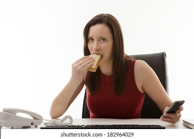 Woman Sitting At Her Desk In The Office Eating A Sandwich As Well As Working On The Go