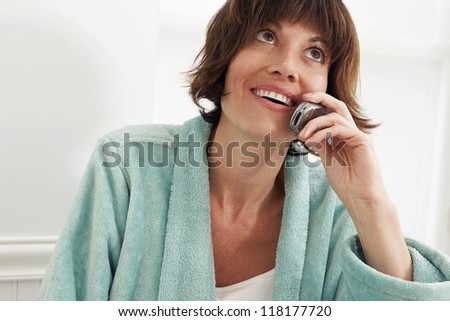 Woman sitting in her towelling bathrobe using a mobile phone and looking up at the ceiling