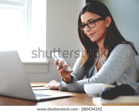 Woman sitting in home office at desk smirking and checking mobile phone.