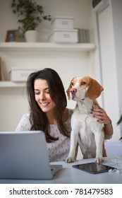 Woman Sitting In Home Office With Her Dog And Using Laptop For Work.
