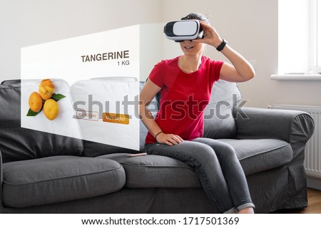 WOman sitting at home on the sofa with vr glasses buying grocery fruit food products.