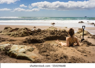 Woman sitting in hot water thermal pool in Hot Water beach in Mercury Bay, Coromandel, New Zealand