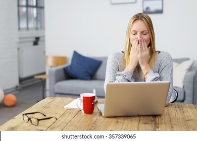 Woman Sitting At Laptop At Home Holding Her Hands On Her Mouth Afraid Of A Computer Virus Or A Mistake