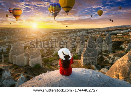 Woman sitting and looking to hot air balloons at sunrise in Cappadocia, Turkey.