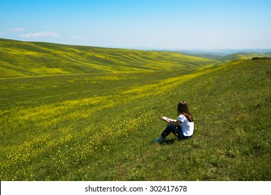 woman sitting and looking at the landscape of hills with yellow flowers