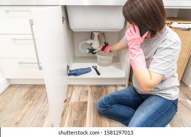 Woman Sitting Near Leaking Sink In Laundry Room Calling For Help