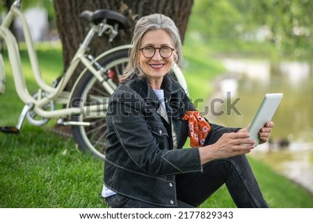 A woman sitting near the river and watching something online