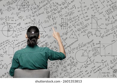 A woman is sitting near a wall with a drawing of mathematical equations, graphs amd diagrams and pointing on it. Idea generating and thinking concept