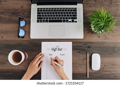 Woman Sitting At Office Desk With Opened Laptop And Filling List Of Party Guests And Gifts For Holiday