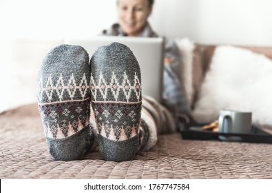 Woman Sitting On Bad In The Badroom With Warm Socks In A Winter Morning. Girl Using Laptop And Working At Home