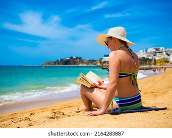 Woman Sitting On Beach In Albufeira, Portugal Reading Book 