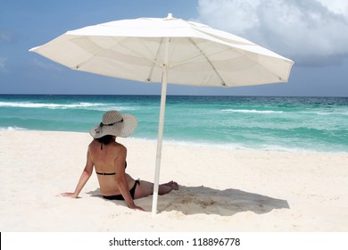 Woman Sitting On A Beach Under The Shade Of An Umbrella.