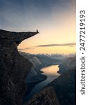 Woman sitting on the beautiful Trolltunga rock, in Norway. Beautiful sunset in the background.