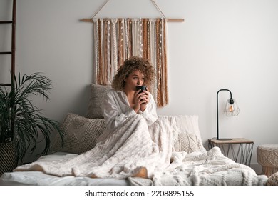 Woman sitting on bed and drinking coffee - Shutterstock ID 2208895155
