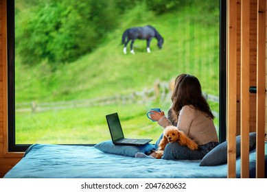 Woman sitting on the bed and looks outside the window seeing mountain. Concept of the workplace at mountain chalet, working remotely. - Powered by Shutterstock