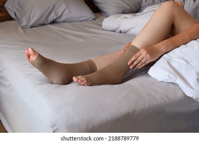 Woman Sitting On Bed Putting On Compression Socks On Her Legs