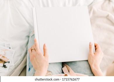 Frau sitzt auf dem Bett mit einem weißen Buchcover, das in Händen aufgetaucht ist. Weiße Buchvorlage. Quadratisches leeres Buch in den Händen der Frau. Arbeiten Sie von zu Hause aus. Büro auf dem Bett. Freiberufler mit einem Buch zu Hause