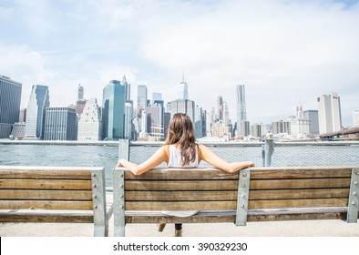 Woman sitting on a bench and looking at New York skyline - Tourist enjoys the view of Manhattan cityscape - Powered by Shutterstock