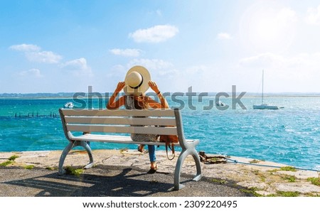 Woman sitting on a bench looking at atlantic ocean and boats- vacation, travel destination, relaxing, summer holiday ( Le croisic in France, Loire atlantic)