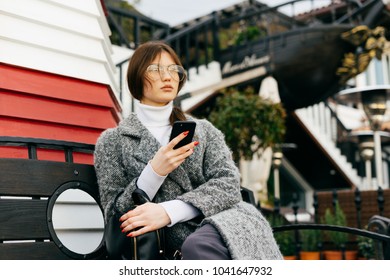 woman sitting on a bench in the park with a phone in hands - Powered by Shutterstock