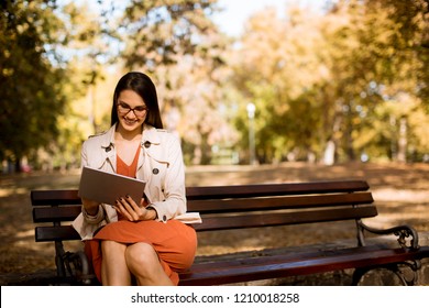 Woman sitting on bench in park during autumn weather using tablet pc and  checking social media. - Powered by Shutterstock