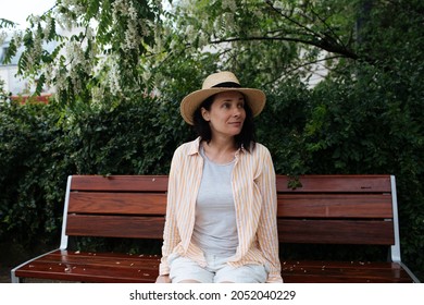Woman sitting on bench in park. Female wearing a hat and bright pastel clothes. Lifestyle portraits in the city park bench