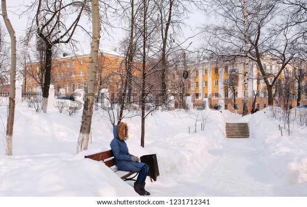 Woman is sitting on bench in winter city park in\
sunny day.
