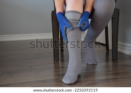 Woman sitting on a chair putting on compression stockings to control lymphedema condition using donning gloves