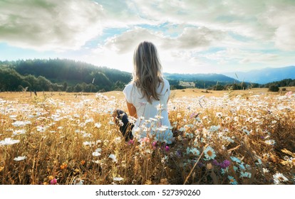 Woman Sitting On The Chamomiles Field And Looking At The Mountain And Sun.