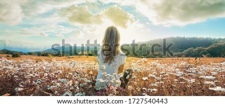 Woman sitting on the chamomiles field and looking at the cloudy sky at sunset. Banner edition.	