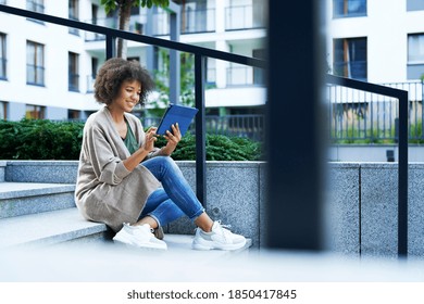 Woman Sitting On City Steps And Scrolling On The Tablet                               