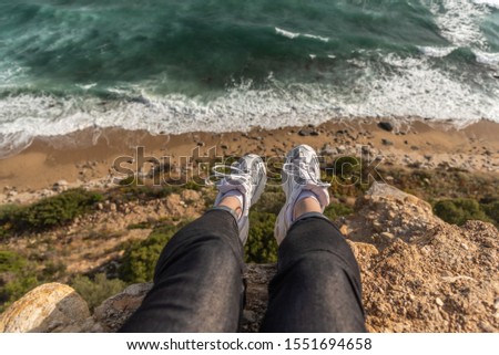 Woman sitting on the cliff above the sea. First person point of view, legs.