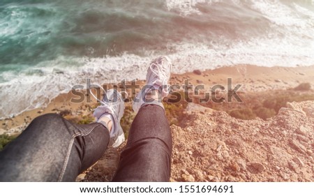 Woman sitting on the cliff above the sea. First person point of view, legs.