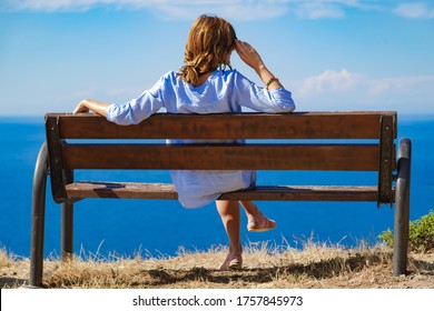 Woman sitting on a cliff bench above ocean / sea.