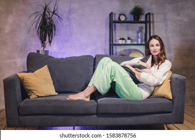 A woman sitting on the couch in a cozy room watching TV and dissatisfied with what she sees on the screen