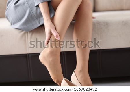 Woman is sitting on couch and holding on to sore leg closeup. Varicose veins of lower leg concept