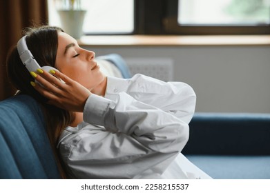 woman sitting on the couch at home listening to music on headphones technologies. - Powered by Shutterstock