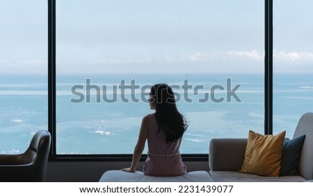 Woman sitting on couch, with ocean view in raining day