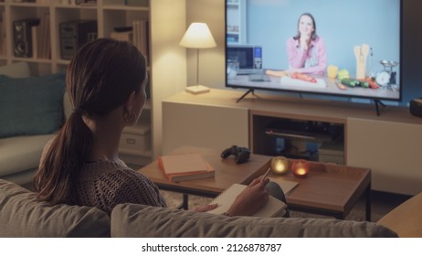 Woman Sitting On The Couch And Watching A Cooking Show On Television, She Is Learning New Recipes