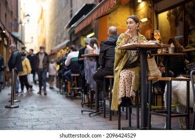 Woman sitting on crowded street at bar or restaurant outdoors in Bologna city. Concept of Italian lifestyle and gastronomy