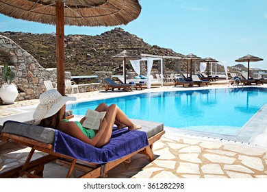 Woman Sitting On A Deck Chair And Reading Her Book On A Swimming Pool