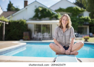 Woman Sitting On Diving Board At Poolside