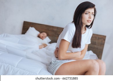 Woman Sitting On Edge Of Bed And Holding Stomach