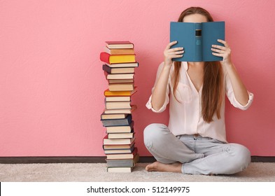 Woman sitting on a floor and holding book in front of face on pink background