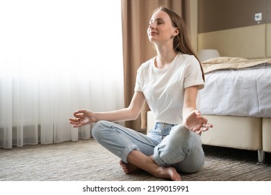 Woman Sitting On Floor In Hotel Room Meditates Feeling Surge Of Power. Adult Tourist Sits In Yoga Pose To Calm Down And Vanish Negativity From Body