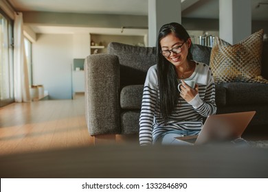 Woman Sitting On Floor Laptop And Coffee Looking At Book. Smiling Asian Female Relaxing At Home.