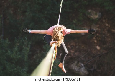 A woman is sitting on a highline, Highliner on a stretched sling, The girl does stretching on a sling stretched over the forest, Trying to get up, highlining, A tightrope walker catches a balance.