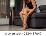 Woman sitting on home sofa, touching ankle, feeling ache, pain, suffering from heavy legs, vein, joints disease. People and healthcare concept