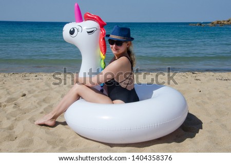 Woman sitting on inflatable rainbow unicorn pool tube on beach sand near sea
