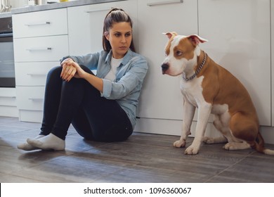 Woman sitting on the kitchen floor mad on her dog who is sad